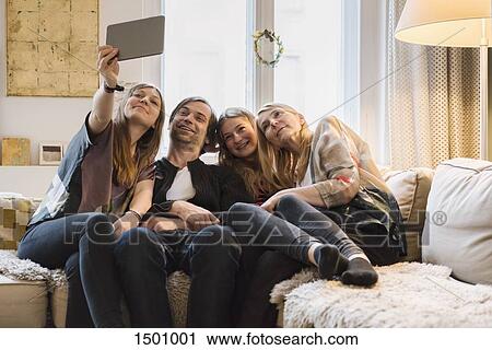 Stock Image - Happy family of four taking selfie through digital tablet at home. Fotosearch