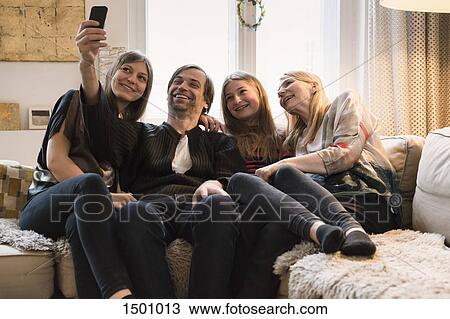 Stock Image - Happy family of four talking selfie through mobile phone at home. Fotosearch