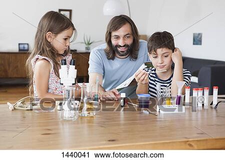 Stock Image - Happy father and children doing school science project at home. Fotosearch