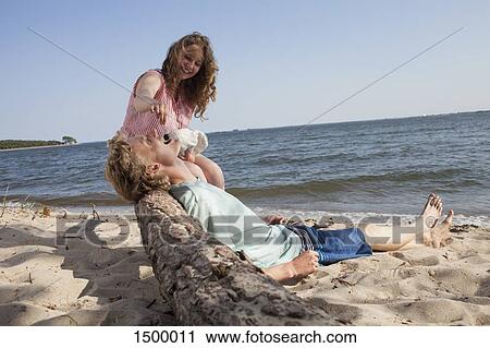 Stock Image - Happy friend feeding cherry to man while relaxing at beach. Fotosearch