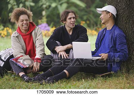 Happy friends relaxing below tree on grassy field at park View Large Photo Image Stock Photo - Happy friends relaxing below tree on grassy field at park. Fotosearch