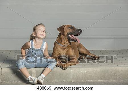 Stock Photo - Happy girl sitting with dog on sidewalk outdoors. Fotosearch