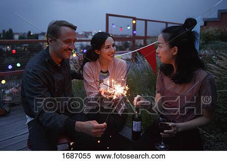 Stock Photography - Happy male and female friends holding sparklers on patio. Fotosearch