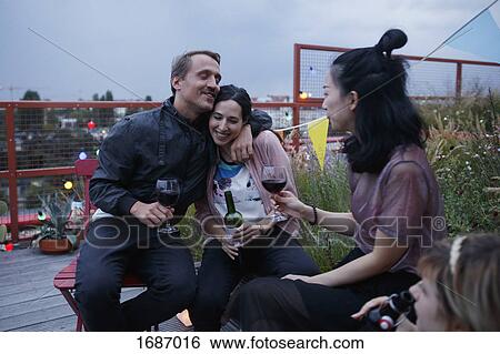 Happy man embracing woman while sitting with friends on patio at dusk View Large Photo Image Stock Photograph - Happy man embracing woman while sitting with friends on patio at dusk. Fotosearch