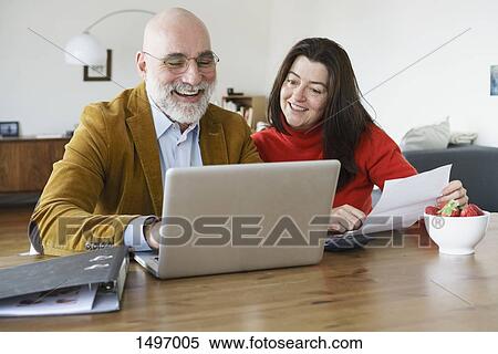 Stock Photography - Happy mature couple using laptop on table at home. Fotosearch