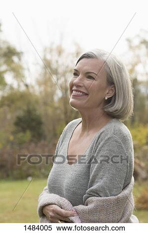 Stock Photography - Happy mature woman looking away while standing at park during autumn. Fotosearch
