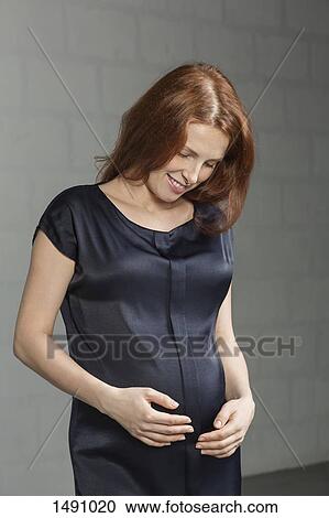 Happy mid adult pregnant woman looking at stomach against gray background View Large Photo Image Stock Image - Happy mid adult pregnant woman looking at stomach against gray background. Fotosearch