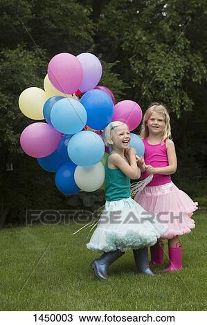 Stock Image - Happy siblings holding balloons in backyard. Fotosearch