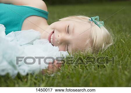 Stock Photo - Happy smiling girl lying on grassy field at backyard. Fotosearch