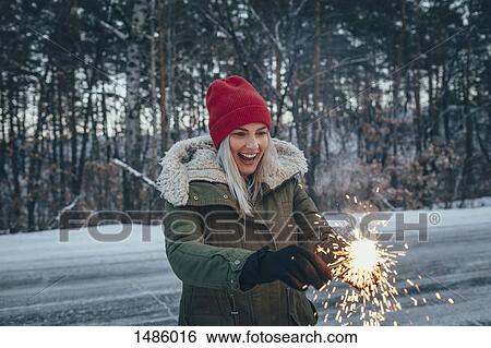Happy woman holding sparklers while standing on field during winter View Large Photo Image Stock Photograph - Happy woman holding sparklers while standing on field during winter. Fotosearch