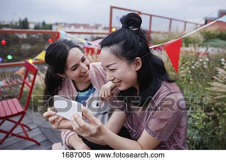 Happy woman looking at female friend using smart phone on patio View Large Photo Image Stock Photography - Happy woman looking at female friend using smart phone on patio. Fotosearch