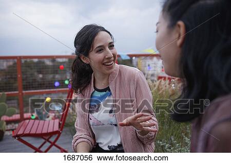 Stock Photograph - Happy woman talking to female friend while sitting on patio. Fotosearch