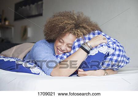 Happy woman with closed eyes holding pillow while lying on bed at home View Large Photo Image Stock Image - Happy woman with closed eyes holding pillow while lying on bed at home. Fotosearch