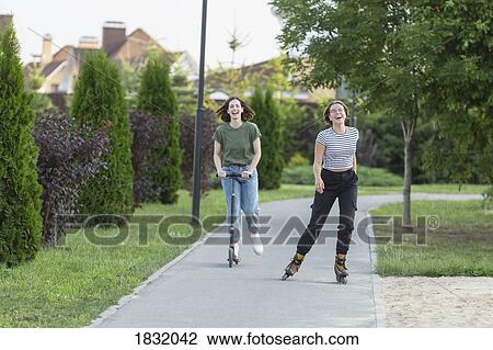Happy women friends rollerblading and riding push scooter on sidewalk View Large Photo Image Stock Image - Happy women friends rollerblading and riding push scooter on sidewalk. Fotosearch