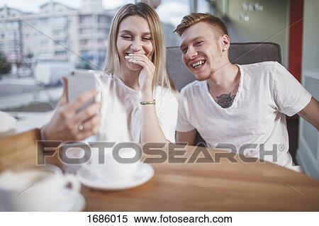 Happy young couple looking at mobile phone while sitting at restaurant View Large Photo Image Stock Photography - Happy young couple looking at mobile phone while sitting at restaurant. Fotosearch