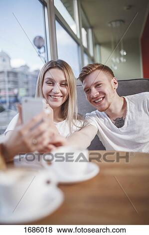 Happy young couple taking selfie with mobile phone while sitting at restaurant View Large Photo Image Stock Photo - Happy young couple taking selfie with mobile phone while sitting at restaurant. Fotosearch