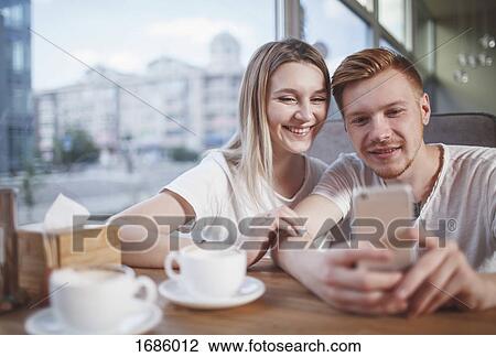 Happy young couple using mobile phone while sitting at restaurant View Large Photo Image Stock Image - Happy young couple using mobile phone while sitting at restaurant. Fotosearch