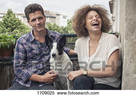 Happy young friends sitting with dog in balcony View Large Photo Image Stock Photography - Happy young friends sitting with dog in balcony. Fotosearch