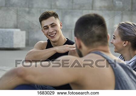 Happy young male athlete gesturing while resting with friends on footpath View Large Photo Image Stock Photo - Happy young male athlete gesturing while resting with friends on footpath. Fotosearch