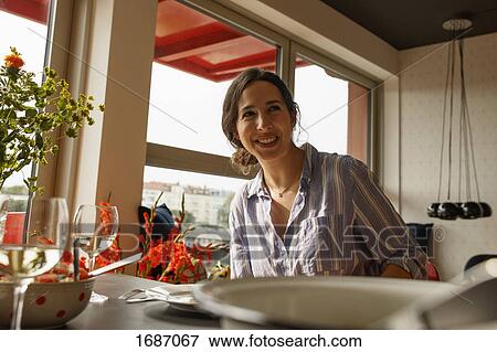 Stock Photo - Happy young woman looking away while sitting at dining table. Fotosearch