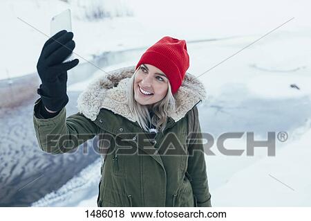 Happy young woman taking selfie on smart phone during winter View Large Photo Image Stock Photo - Happy young woman taking selfie on smart phone during winter. Fotosearch