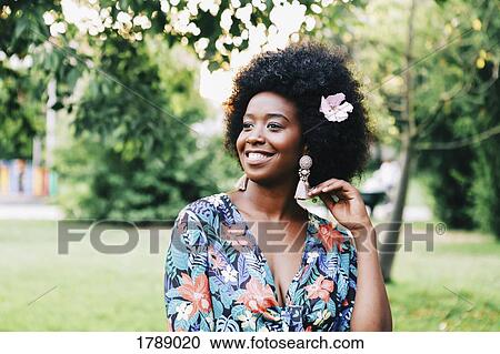 Stock Image - Happy young woman with pink flower in hair. Fotosearch