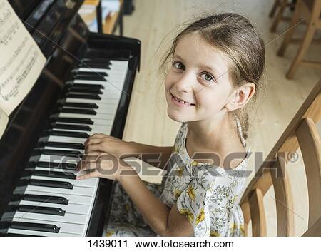 Stock Image - High angle portrait of girl playing piano at home. Fotosearch