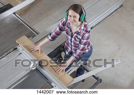 Stock Photo - High angle portrait of happy female carpenter using a sliding table saw in workshop. Fotosearch