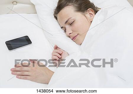 Picture - High angle view of beautiful woman sleeping with smart phone on pillow in bed. Fotosearch