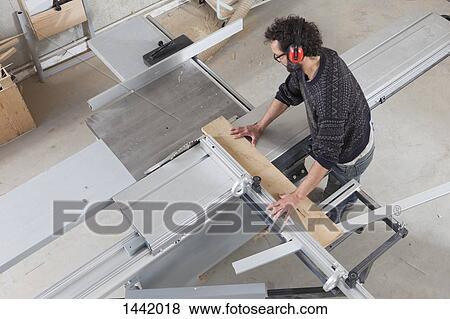Stock Photo - High angle view of carpenter using a sliding table saw in workshop. Fotosearch
