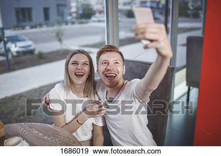 High angle view of happy young couple taking selfie with mobile phone while sitting at restaurant View Large Photo Image Stock Photo - High angle view of happy young couple taking selfie with mobile phone while sitting at restaurant. Fotosearch