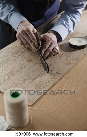 Stock Photograph - High angle view of man rubbing leather belt on wooden table. Fotosearch