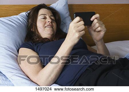 High angle view of mature woman lying on bed and using smart phone View Large Photo Image Picture - High angle view of mature woman lying on bed and using smart phone. Fotosearch