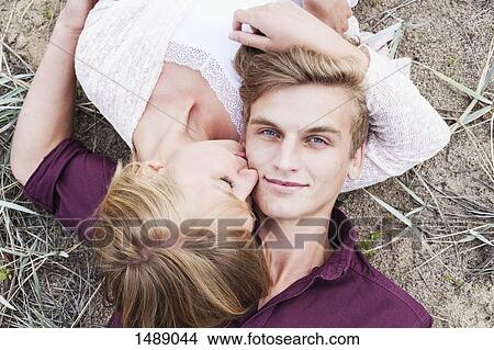 Picture - High angle view of woman kissing man while lying on field. Fotosearch