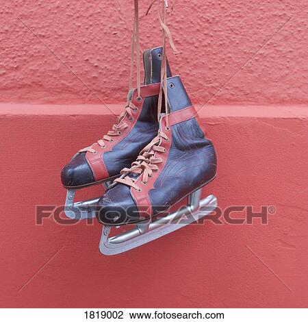 Stock Image - Ice skates hanging against red wall. Fotosearch