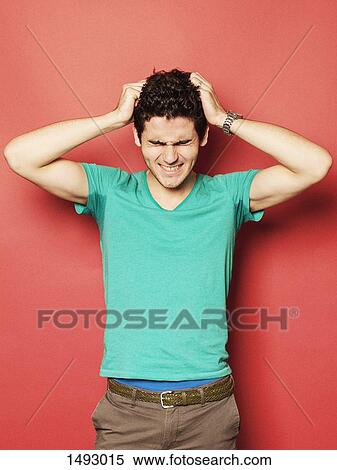 Stock Photography - Irritated young man pulling hair against red background. Fotosearch