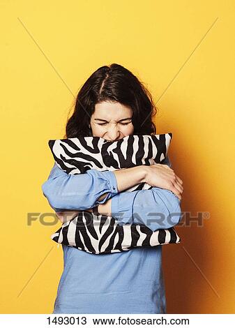 Stock Image - Irritated young woman embracing cushion against yellow background. Fotosearch