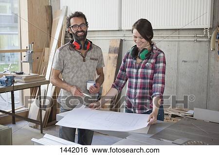 Stock Photograph - Laughing male and female carpenters with blueprint in workshop. Fotosearch