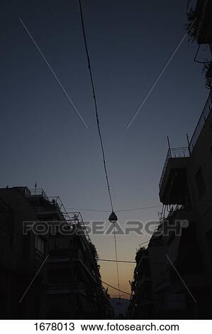 Stock Image - Low angle view of cables amidst buildings in silhouette against clear sky at dusk. Fotosearch