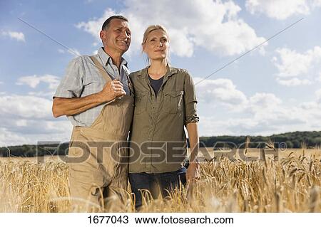 Low angle view of mature couple standing amidst crops at farm against sky on sunny day View Large Photo Image Stock Image - Low angle view of mature couple standing amidst crops at farm against sky on sunny day. Fotosearch