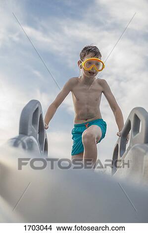 Low angle view of shirtless boy wearing swimming goggles on water slide against sky View Large Photo Image Picture - Low angle view of shirtless boy wearing swimming goggles on water slide against sky. Fotosearch