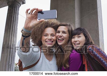 Low angle view of smiling young female friends taking selfie View Large Photo Image Picture - Low angle view of smiling young female friends taking selfie. Fotosearch