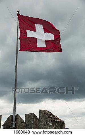 Stock Image - Low angle view of Swiss Flag flapping in wind against cloudy sky. Fotosearch