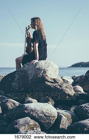 Low angle view of woman with violin sitting on rocks by lake while looking away View Large Photo Image Stock Image - Low angle view of woman with violin sitting on rocks by lake while looking away. Fotosearch