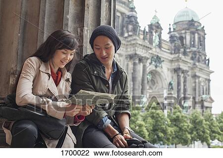 Stock Image - Low angle view of young friends reading map at Altes Museum against Berlin Cathedral, Germany. Fotosearch