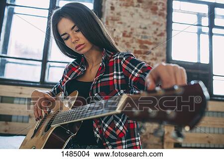 Low angle view of young woman playing guitar at home View Large Photo Image Picture - Low angle view of young woman playing guitar at home. Fotosearch