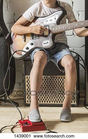 Stock Image - Low section of boy playing guitar at home. Fotosearch