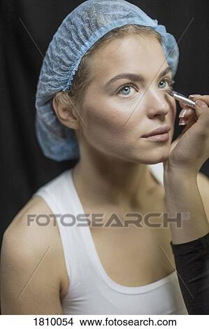 Picture - Makeup artist applying makeup to eyes of young woman in shower cap. Fotosearch