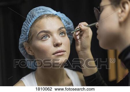 Stock Image - Makeup artist applying makeup to eyes of young woman wearing shower cap. Fotosearch