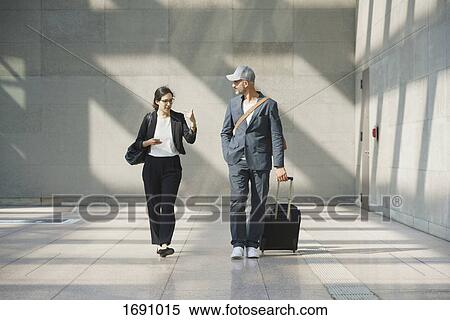 Stock Photography - Male and female business colleagues talking while walking at airport. Fotosearch